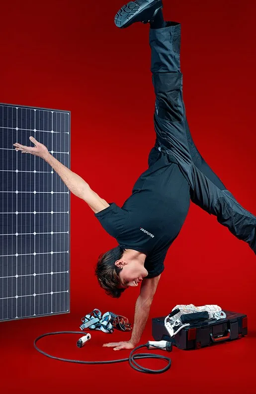 Mitarbeiter macht vor rotem Hintergrund einen Handstand neben einem Photovoltaikmodul