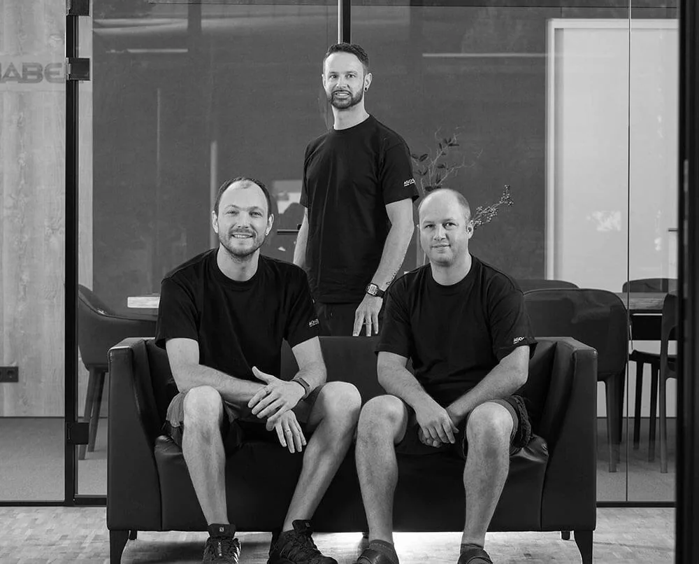 Drei Mitarbeiter in schwarzen T-Shirts auf einem Sofa, schwarz-weiß